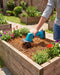 Seesii 20V teal mini cordless tiller cultivating soil in wooden raised flower bed with colorful flowers, lightweight handheld garden rototiller